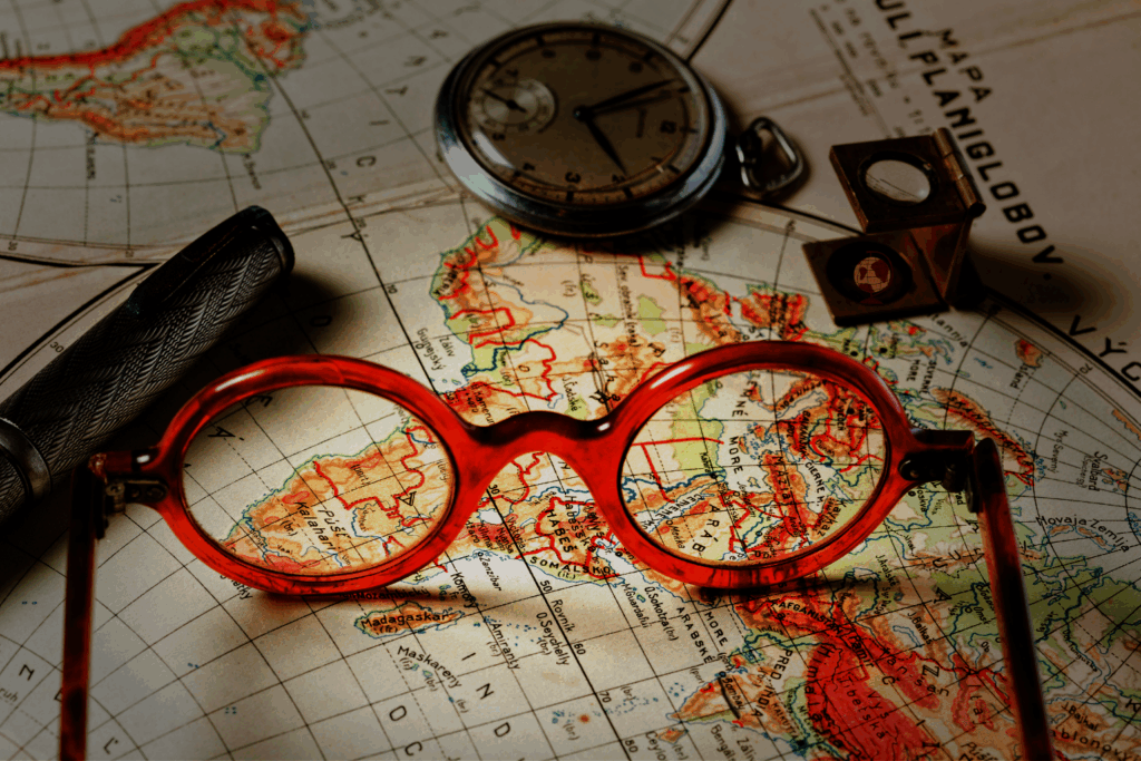 Nahaufnahme einer historischen Weltkarte mit Brille, Taschenuhr, Füllfederhalter und Messinstrument